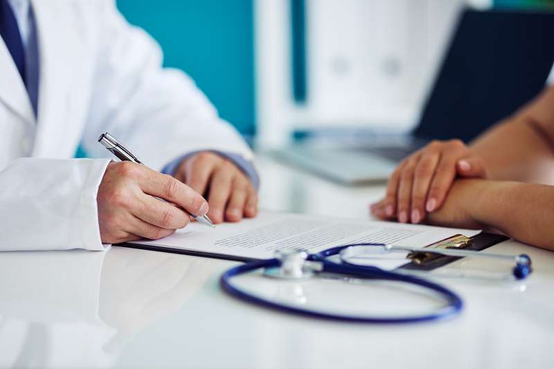 Male doctor consults with his patient and writes notes on the clipboard